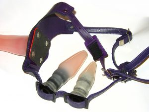 strap-on play for all genders workshop strap on harness pegging [Image Description - black leather and nylon strap on harness featuring two plugs. The back plug is smaller than the front. Both are beige/flesh tone and have slightly ribbed bases]